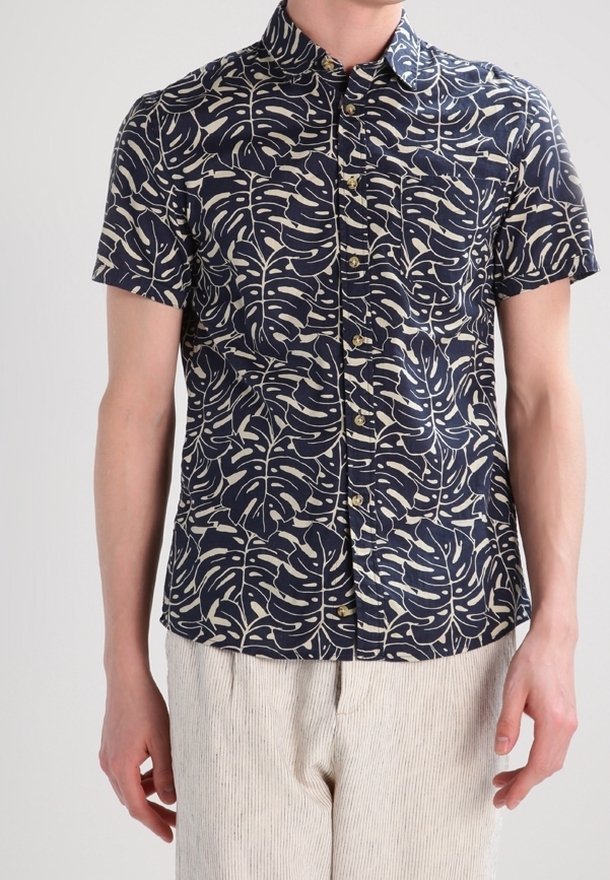Camicia a maniche corte di colore blu navy con un motivo fogliare bianco. Presenta un colletto con bottoni e cinque bottoni frontali, realizzata in un tessuto leggero.
