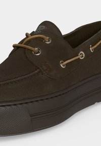 Chaussure bateau décontractée en daim brun foncé avec des lacets en cuir fauve passés dans des œillets métalliques et une semelle en caoutchouc texturée.