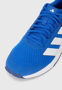Blue athletic shoe with a mesh upper, textured surface, and white stripe accents. Features blue laces and a rubber sole.