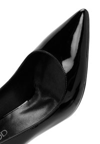 Zwarte lakleren pump met een spitse neus en uitsnijdingen. Heeft een gladde textuur en een glanzende afwerking.