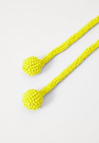 Gul perleaccessory med to runde, strukturerede kugler på forlængede, rørformede tråde. Lavet af glat plastmateriale med en levende finish.