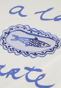 Keramische schaal met handgeschilderd ontwerp van blauwe vissen in een ovale lijst, omrand door een gekartelde rand en een gestippelde lijn. De achtergrond is wit.