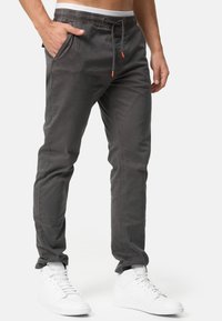 Pantalones jogger de algodón gris con cintura elástica, detalle de cordón, bolsillos laterales y un corte ajustado. Llevados con zapatillas blancas.