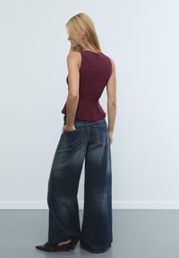 Top peplum bordeaux senza maniche abbinato a jeans larghi in denim blu scuro, con ampie tasche posteriori e finitura scolorita.