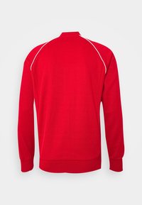 Röd lättvikts sweatshirts med långa ärmar, försedd med vita accentlinjer på axlarna och en hög krage. Slät texturerad tyg.