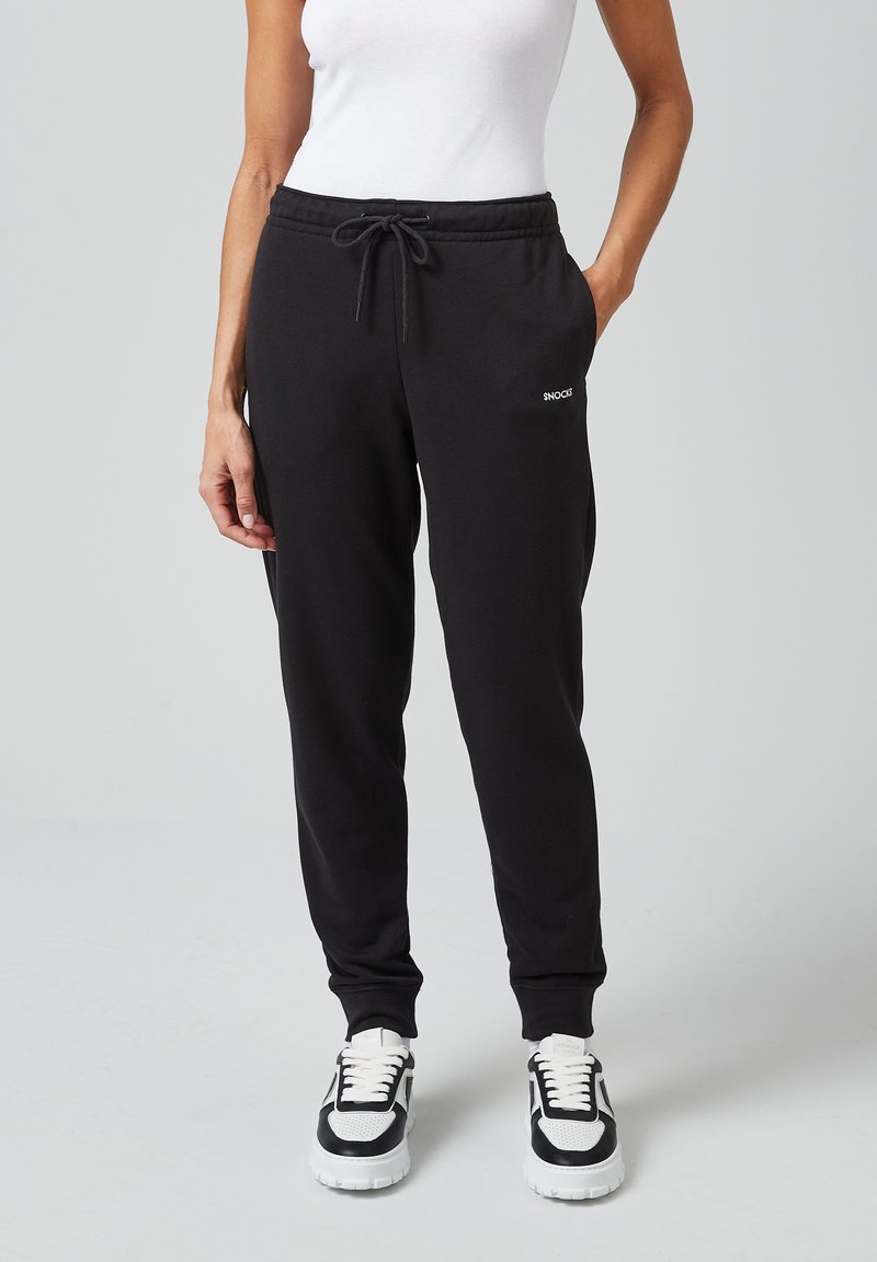 Zwarte sweatpants gemaakt van een zachte stof met een elastische tailleband, koord en zijzakken; voorzien van een klein wit logo aan de linkerkant.