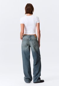 Φαρδιά τζιν παντελόνια από ανοιχτό μπλε ντένιμ με ξεθωριασμένο φινίρισμα. Διαθέτουν μεγάλες πίσω τσέπες και δερμάτινο ταμπελάκι στη μέση. Λευκό εφαρμοστό t-shirt.