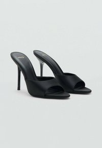 Mulas negras de tacón alto hechas de material sintético liso, con punta abierta y un diseño recortado con un tacón metálico elegante.