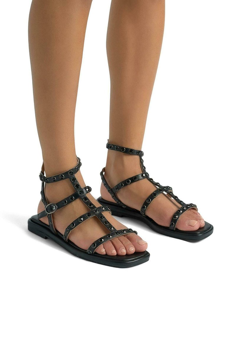 Zwarte sandaaltjes met bandjes en zilveren studs, vlakke zool en open teen ontwerp, met meerdere bandjes over de voet en enkel.