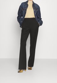 Veste en denim, haut beige, pantalon noir tailleur et chaussures à talons à motifs avec des accents jaunes et noirs. Coupe structurée et design à jambe droite.