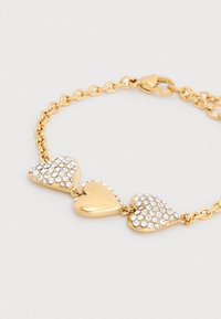 Βραχιόλι σε χρυσό τόνο με τρεις συνδέσμους σε σχήμα καρδιάς. Δύο καρδιές διακοσμημένες με διάφανα στρας, με υφή στην επιφάνεια. Ασφαλές κούμπωμα.