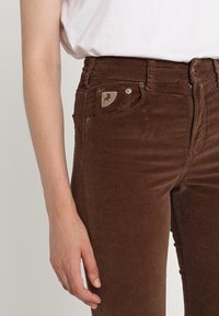 Bruna manchesterbyxor med en smal passform, med en sidficka med ett etikettmärke, metallknappsstängningar och en subtil ribbad textur.