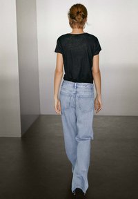 Zwarte short-sleeve t-shirt gecombineerd met lichtblauwe tapered jeans, met riemlussen en achterzakken, gezien vanaf de achterkant.