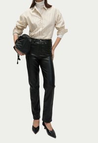 Beige randig skjorta med knappar och uppvikta ärmar, kombinerad med svarta läderbyxor. Modellen håller en svart väska och har på sig svarta klackskor med spetsig tå.