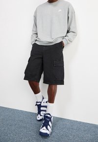Grå sweatshirt med rund hals, svarta cargoshorts med sidfickor och blå-vita sneakers med "AIR" tryckt på sidan.
