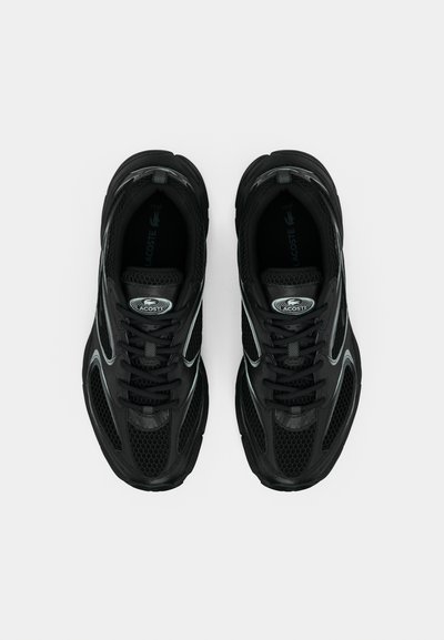 Chaussures de sport noires avec dessus en maille, semelle en caoutchouc et accents gris contrastants. Présentent une forme arrondie et une fermeture traditionnelle à lacets.