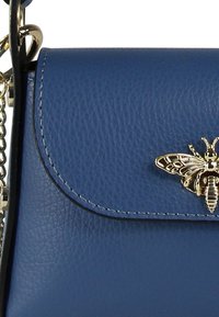 Sac à main en cuir bleu avec une finition texturée, doté d'un fermoir en forme d'abeille dorée et d'une bandoulière en chaîne. Forme rectangulaire compacte.