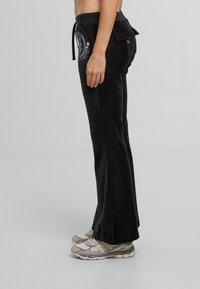 Czarne rozszerzane spodnie z miękkiego materiału mają elastyczny pasek w talii oraz tylną kieszeń z małym haftowanym wzorem po lewej stronie.