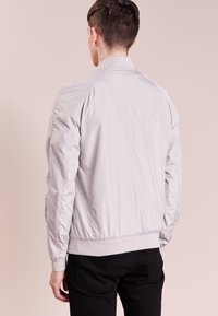 Chaqueta bomber gris claro con textura suave, puños y cinturilla acanalados; cuenta con mangas raglán y un diseño liso en la parte trasera.