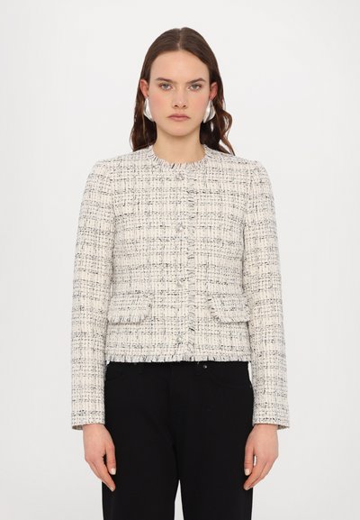 Weißes und schwarzes Tweed-Jackett mit einem cropped Design, rundem Halsausschnitt, Knopfverschluss vorne und zwei aufgesetzten Taschen. Texturiert mit fransigen Kanten.