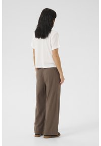 Witte shirt met korte mouwen, gecombineerd met loszittende, bruine stoffen broek met een elastische tailleband en een ontspannen silhouet.