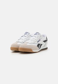 Hvite sporty sneakers med grå suedetåhette, svarte detaljer og såle av gummi. Har flate lisser og logo på tungen.