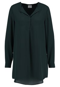 Mörkgrön, långärmad blus i slätt tyg. Har en v-ringning och en något längre bakdel med upprullade manschetter. Inga synliga knäppningar.