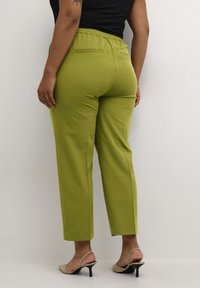 Zelené slim fit kalhoty s elastickým pasem, se zadními kapsami. Materiál má hladkou texturu. V kombinaci s béžovými podpatky.