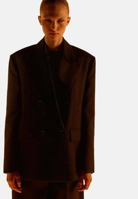 Blazer negro de doble abotonadura en mezcla de lana, con grandes solapas, dos bolsillos frontales y hombros estructurados para un ajuste entallado.