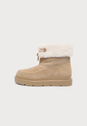 Botte d’hiver en daim beige avec semelle épaisse marron, col en fausse fourrure blanche, coutures décoratives et détail à bascule sur le côté.