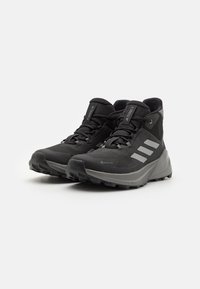 Czarne buty trekkingowe wykonane z wytrzymałego materiału tekstylnego z szarymi akcentami, wyróżniające się wysokim krojem, teksturowaną podeszwą i potrójnym logo.
