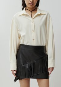 Ivory blouse met lange mouwen en knoopsluiting, gecombineerd met een zwarte leren minirok met franjerand.