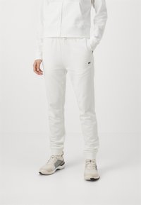 Pantalons de jogging blancs en coton avec taille élastique et poches, assortis à des chaussures de sport de couleur claire avec des accents à motifs.
