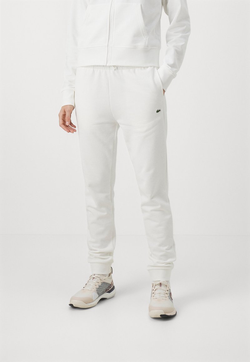 Pantalons de jogging blancs en coton avec taille élastique et poches, assortis à des chaussures de sport de couleur claire avec des accents à motifs.