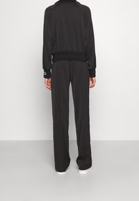 Completo tuta nera composto da giacca aderente con polsini a costine e pantaloni dalla vestibilità comoda. Tessuto morbido con una leggera lucentezza e silhouette allungata.