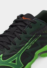 Κλείσιμο σε μαύρο και πράσινο αθλητικό παπούτσι με μαύρα κορδόνια, πορτοκαλί λογότυπο στη γλώσσα και το κείμενο «Wave Lightning Elite» στο πλάι.