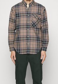 Ruskea ja musta ruudullinen napitettava paita, jossa vihreät yksityiskohdat, rintatasku, kauluksellinen pääntie ja pitkät hihat. Valmistettu pehmeästä kankaasta.