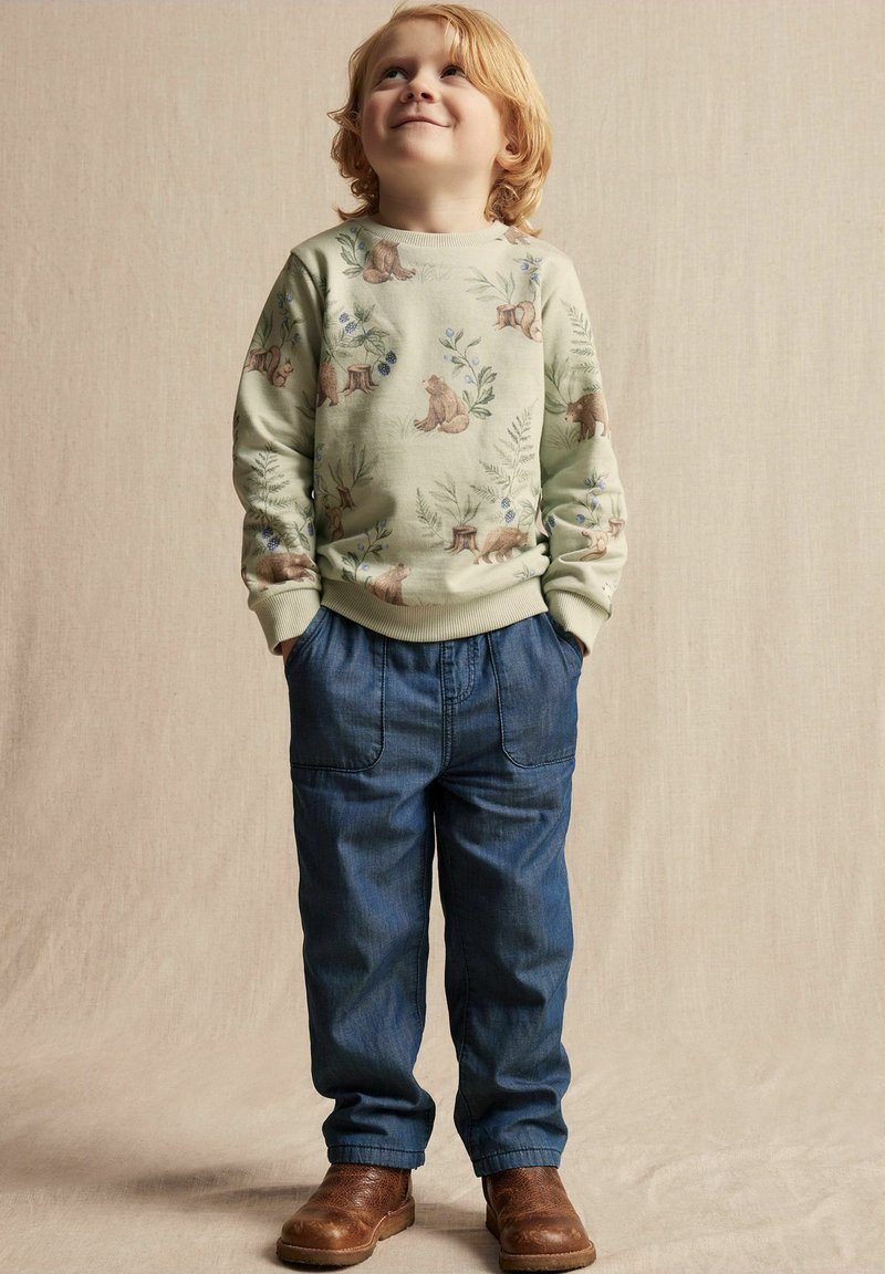 Vaaleanvihreä huppari, jossa on karhun ja lehtien kuvio, yhdistettynä sinisiin farkkuihin. Ruskeat saappaat viimeistelevät asun. Rentoa tyyliä ja teksturoitua kangasta.