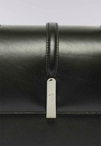 Primo piano di una borsa in pelle nera con una texture liscia, una chiusura magnetica e un accento argento con incisione del logo.