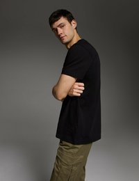 Czarna koszulka z krótkim rękawem ma okrągły dekolt i luźny krój. Noszona z oliwkowo-zielonymi spodniami cargo, które mają kieszenie i teksturowany materiał.