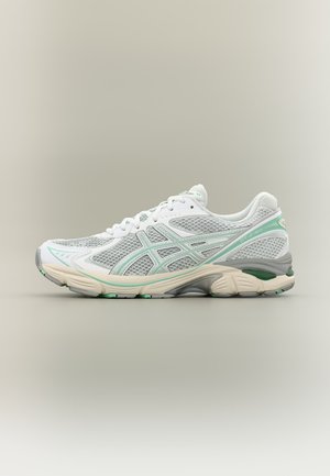 Witte en lichtgroene mesh hardloopschoen met gedempte zool en merkzijdenstrepen, getoond vanaf de buitenkant op een neutrale achtergrond.