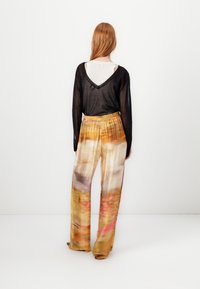 Svart, genomskinlig långärmad topp med V-ringning och avslappnad passform, kombinerad med färgglada, vida mönstrade byxor i mjukt tyg.