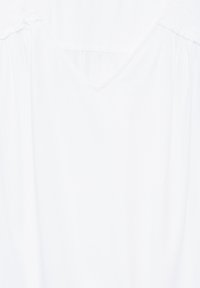 Top in cotone bianco con scollatura a V e spalle arricciate, caratterizzato da una texture liscia e una vestibilità comoda. Design semplice, senza ulteriori motivi o dettagli.