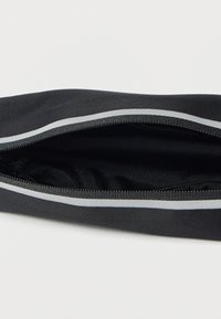 Μαύρη κορδέλα με απαλή υφή, με κλείσιμο φερμουάρ και αντανακλαστικές γκρι λεπτομέρειες κατά μήκος των άκρων.