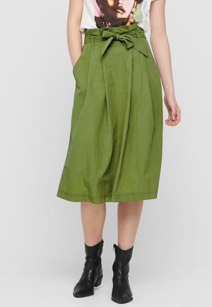 Groene midi-rok van gerimpeld stof, met een strikdetail aan de voorkant, plooien en zijzakken. Draagt bijpassende zwarte enkellaarzen.