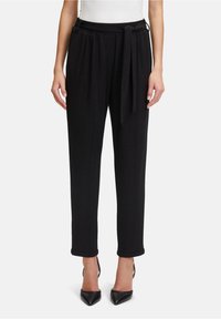 Zwarte taps toelopende broek met een zachte textuur, voorzien van een gestrikt middel en opgerolde manchet, gecombineerd met puntige zwarte hakken.