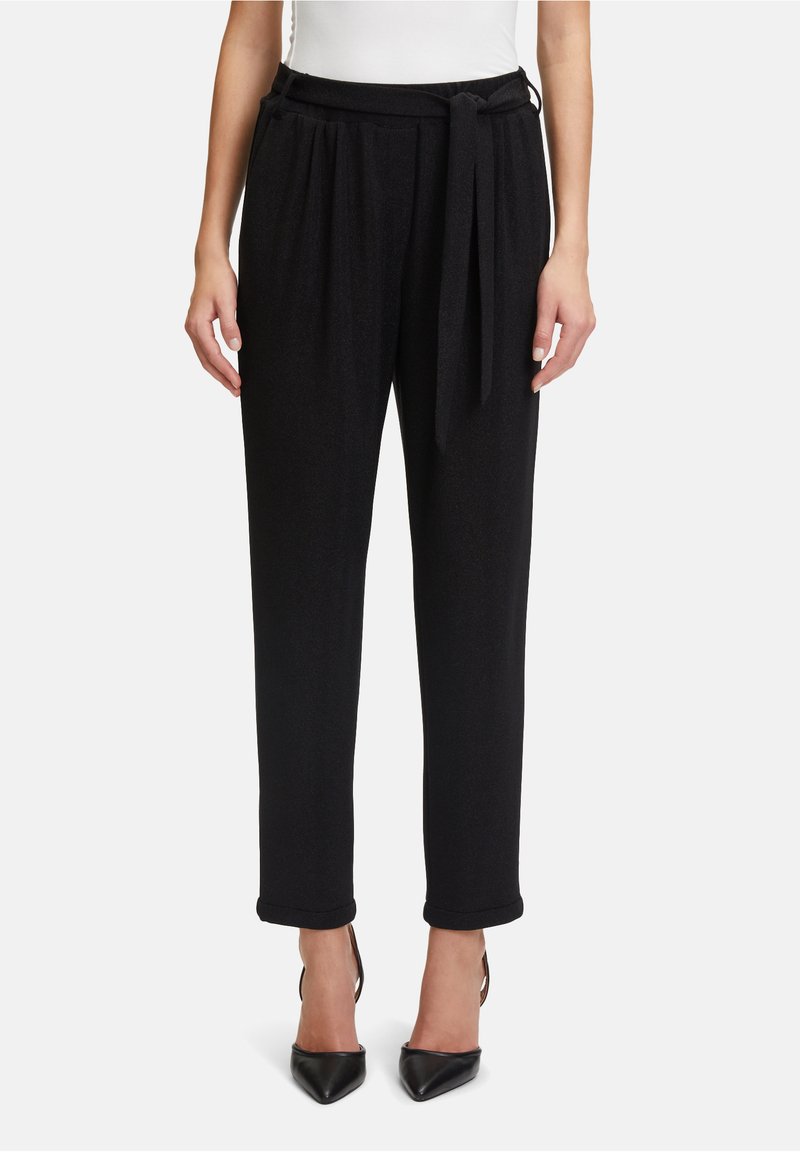 Zwarte taps toelopende broek met een zachte textuur, voorzien van een gestrikt middel en opgerolde manchet, gecombineerd met puntige zwarte hakken.