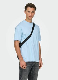 Light blue cotton T-shirt with a round neckline, paired with dark jeans and a black crossbody bag. The fabric appears soft and smooth.