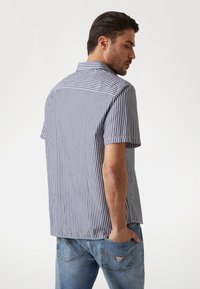 Camisa de manga corta a rayas verticales en navy y blanco, fabricada en un tejido ligero, con un cuello de punta y detalle de costura en el yugo trasero.