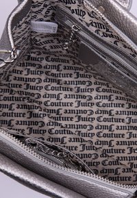 L'interno della borsa a tracolla argentata presenta una fodera a fantasia con "Juicy Couture" stampato in nero. Include un compartimento con zip.
